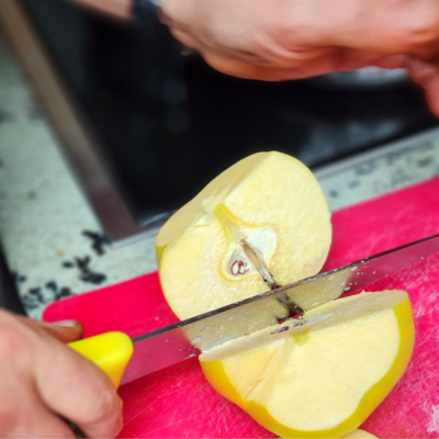 Momentaufnahme eines Messers, das gerade durch eine Quitte geschnitten hat. Man sieht das Kerngehäuse und das saftige, hellgelbe Fruchtfleisch.